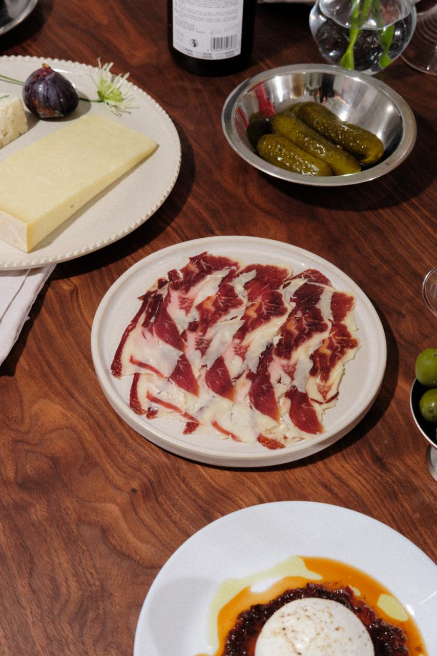 Des tranches de paleta ou épaule de bellota 100% ibérica de la marque LOLO dans une assiette au mileu d'une table